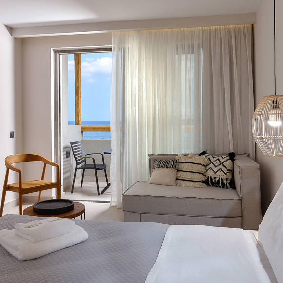 Modern junior suite with a double bed, wall-mounted TV, cozy sitting area and a balcony with side sea view