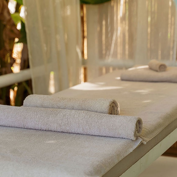 Outdoor massage bed with towels and sheer curtains, surrounded by tropical plants 