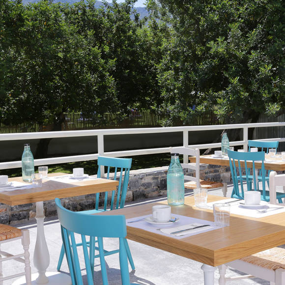 Outdoor dining area of the main restaurant with wooden tables, colorful chairs and garden view