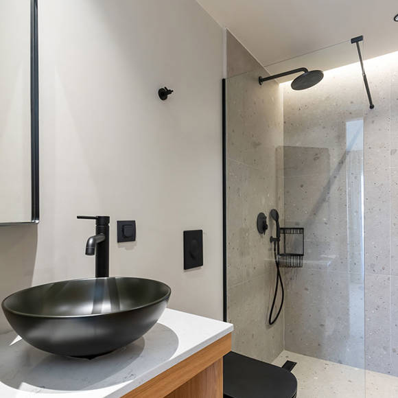 Suite's bathroom with black sink, a mirror, wooden vanity with folded towels and glass shower 