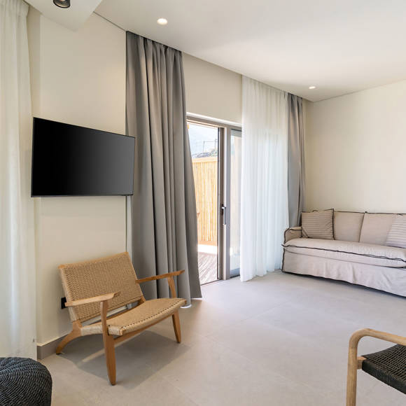 Suite's cozy living room with modern furniture, wall-mounted TV and access to the terrace with the private pool