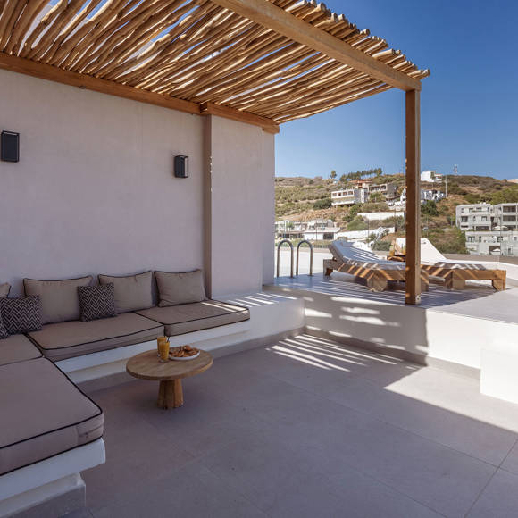 Junior Suite outdoor terrace sitting area shaded by a wooden pergola next to the pool area