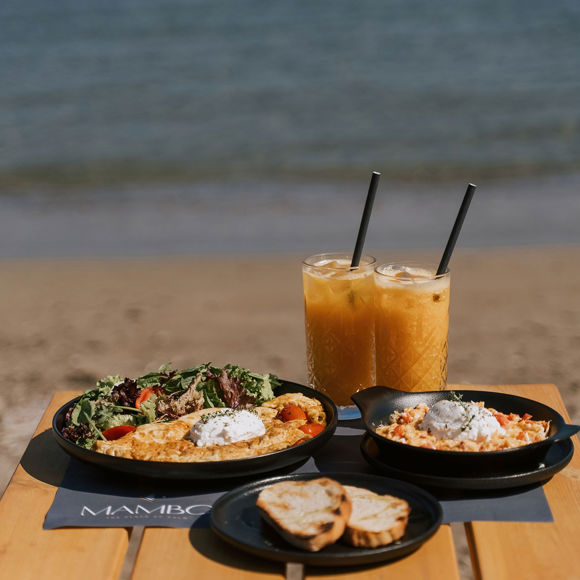 Beachside brunch with salad, omelette, scrambled eggs, fresh bread, and iced juice at Mambo Beach Restaurant