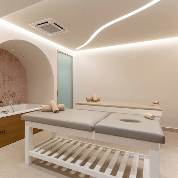 Spa treatment room featuring two massage beds, a built in tub and soft ambient lighting
