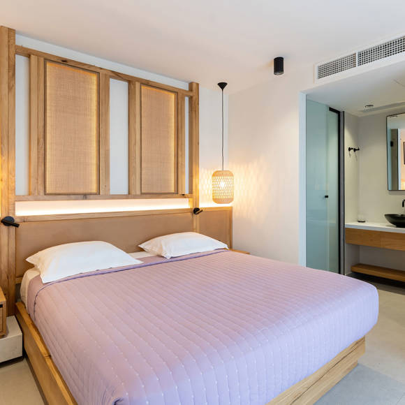 Suite with a king-sized bed, wooden headboard, pendant lights, a glass doored shower and an open black sink with a mirror
