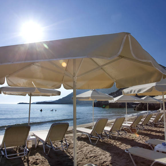 Sandy beach with sunbeds and umbrellas facing the sea under bright summer sun
