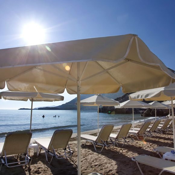 Sandy beach with sunbeds and umbrellas facing the sea under bright summer sun