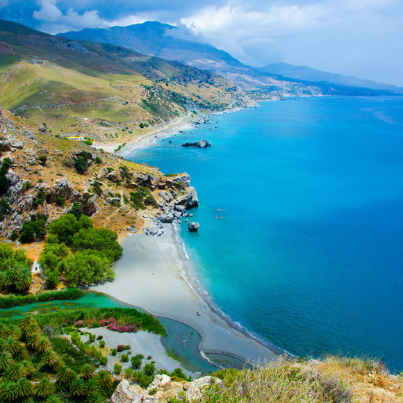 Aerial view of Preveli Beach on Crete with the rive flowing into the sea surrounded by lush green landscape