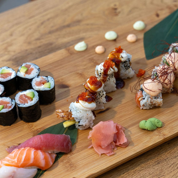 Assorted sushi platter with maki rolls, nigiri, sauces and garnishes on a wooden plate