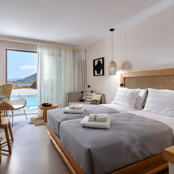 Junior suite with two single beds placed side by side, wooden furniture, seating area and access to pool with side sea view