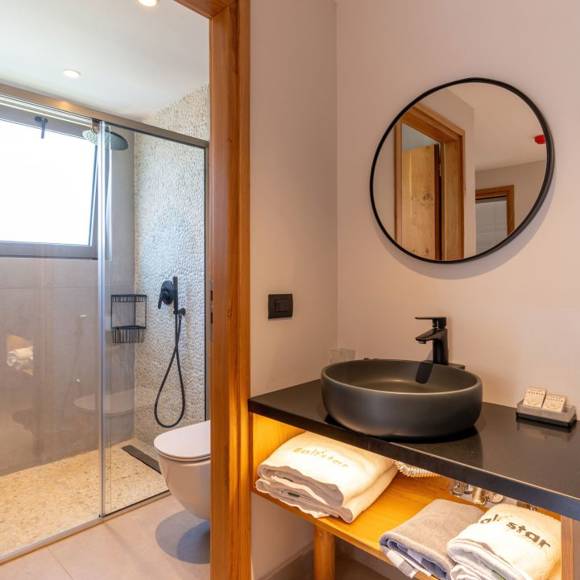Maisonette suite bathroom with black vessel sink, a round mirror, and walk in shower with natural light