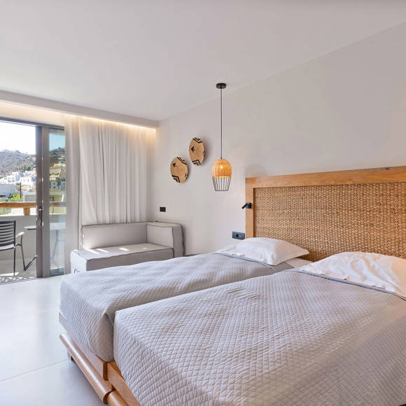 Junior suite with two large single beds side by side, woven headboard, sitting area, and access to a balcony with garden view