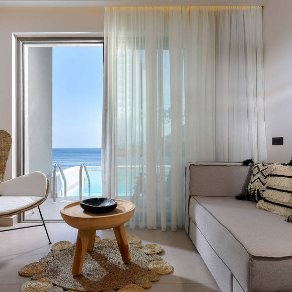 Seating area with sofa, wicker chair, and a round table, overlooking a pool and sea view