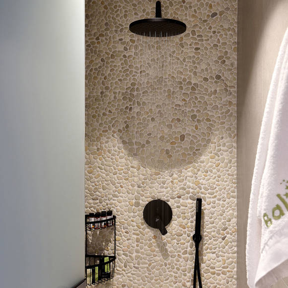 Shower area with pebble wall, black rainfall showerhead and a towel hanging on the side