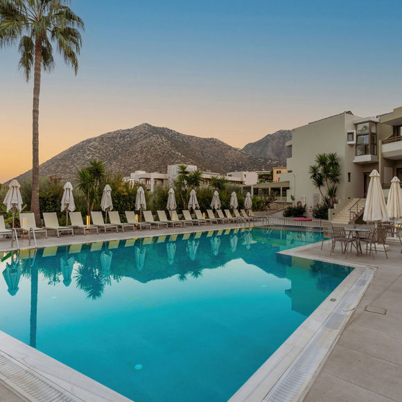 View of the pool with sunbeds lined up on the left and outdoor dining tables on the right