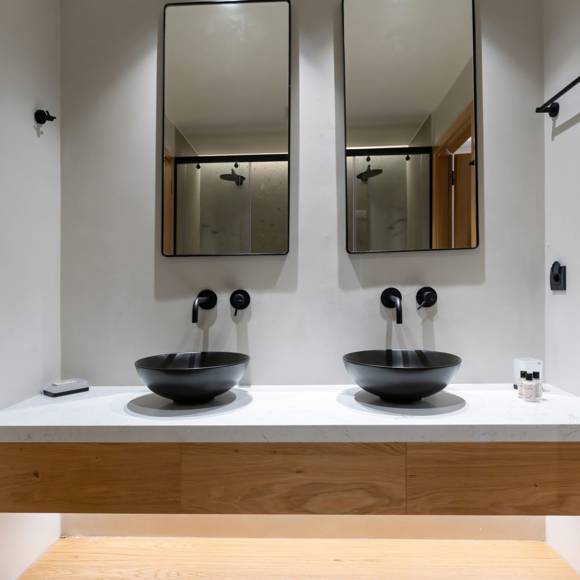 Bathroom with double black vessel sink, wall-mounted faucets and two mirrors above a wooden vanity