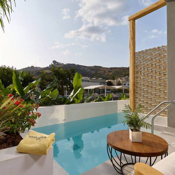 Pool area with a round table, wooden sun lounger, tropical plants and a view of hills