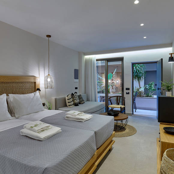 Cozy junior suite with a double bed, a living area, a wall mounted TV, rattan furniture and access to a terrace with greenery
