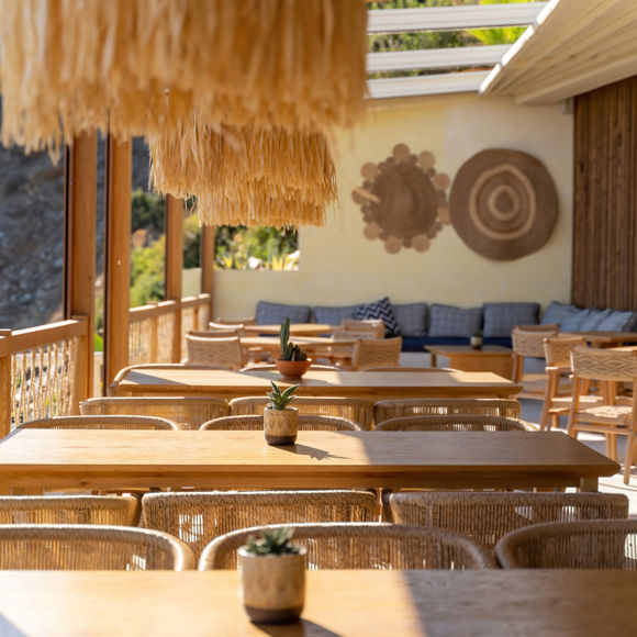 Outdoor seating area of Mambo Beach Restaurant with wooden tables, woven chairs, and natural boho decor