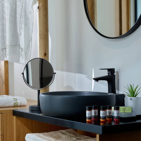 one bedroom suite vanity area with a black sink, round mirrors, toiletries, and wooden furniture with folded towels