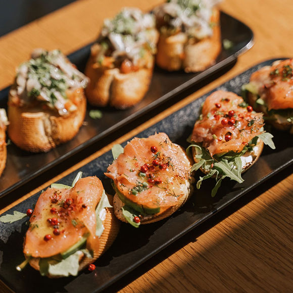 Close-up of a gourmet bruschetta topped with salmon, arugula and cream cheese, served on a black platter