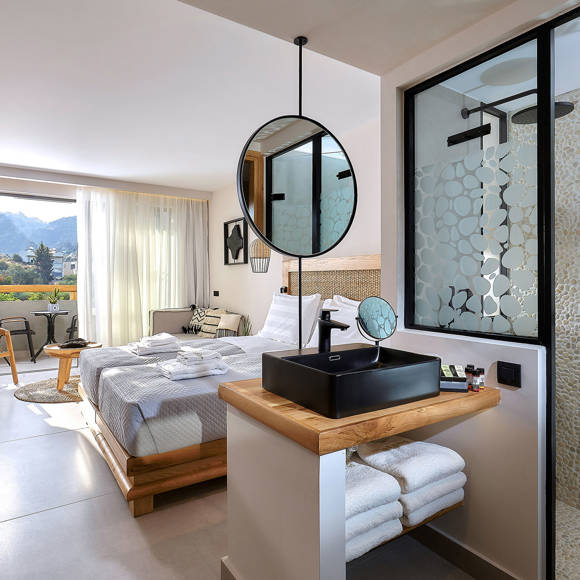 Modern junior suite with a double bed, wooden furniture, open vanity area, and access to a balcony with garden view