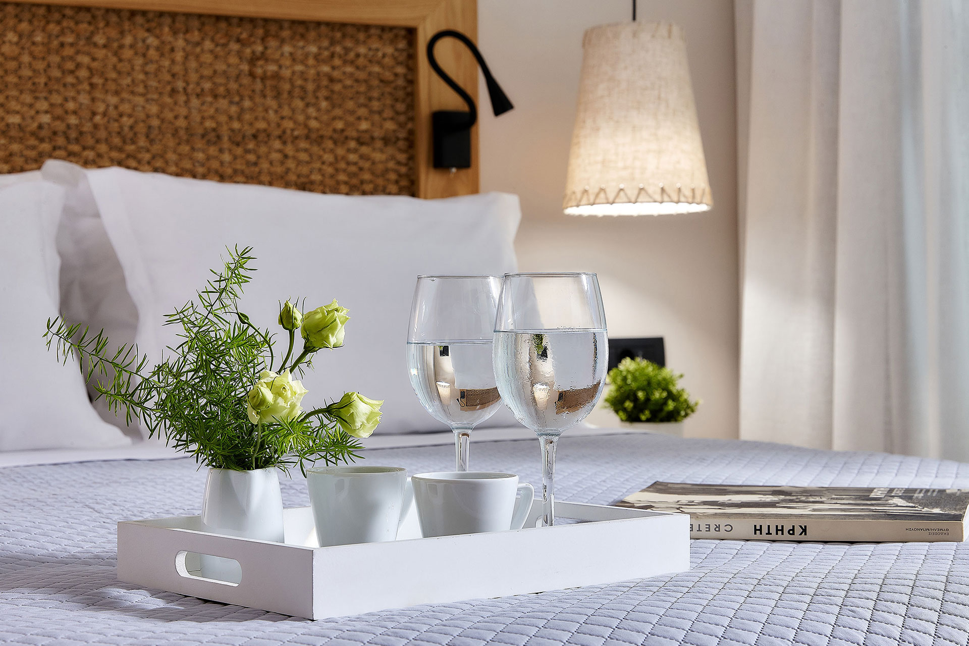 Close-up of a tray with drinks, cups and flowers on a double bed with woven headboard