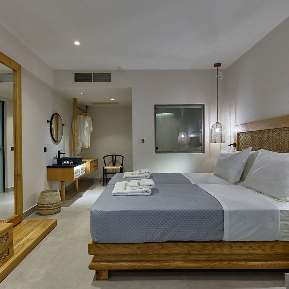 Junior Suite with a double bed with woven headboard, wall-mounted TV, wooden furniture and open-plan bathroom area