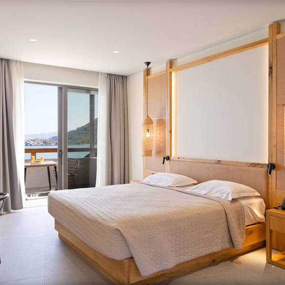 Junior suite with a double bed, wooden furniture, pendant lighting, and a balcony with direct sea view