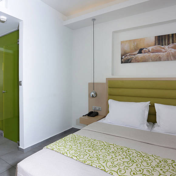 modern room with a double bed with green headboard, wall art above, and a green glass bathroom door nearby