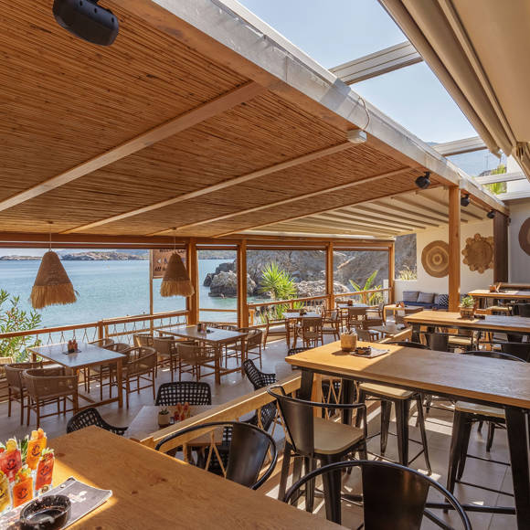 Seafront terrace of Mambo Beach Restaurant with wooden ceiling, boho decor , and panoramic sea view