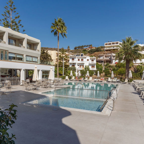 Panoramic view of the pool area, featuring aligned sunbeds, the outdoor dining section and part of the hotel building