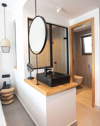 open bathroom area with black sink, round mirrors, a shower room with pebble wall and separate toilet