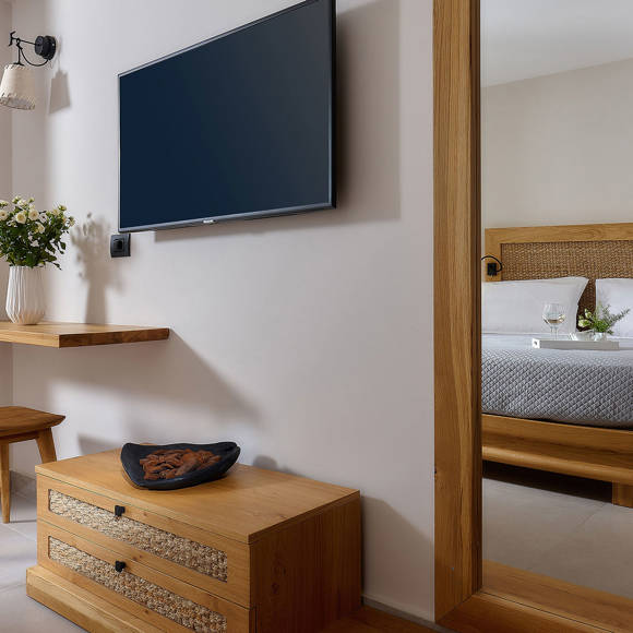 Bedroom with a wall-mounted TV, a wooden desk and chair, and a mirror reflecting a double bed