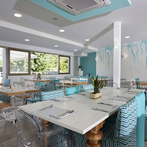 Main restaurant interior with set tables, pastel blue accents and large windows with garden view