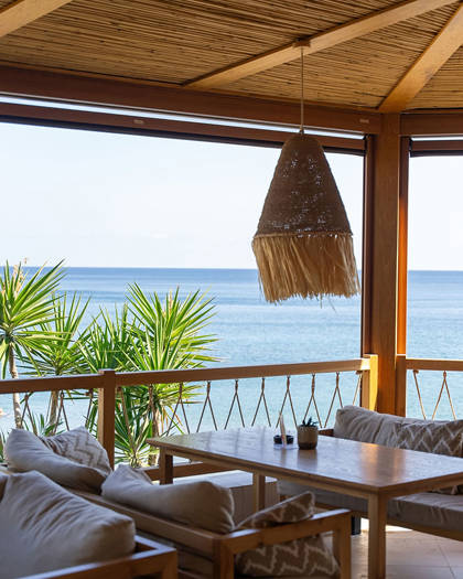 Cozy lounge corner at Mambo Beach Restaurant with sea view, cushioned seating, and woven pendant light