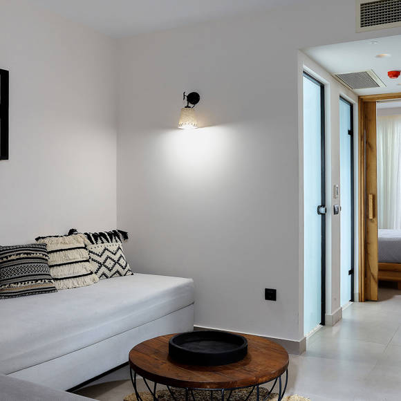 One bedroom suite with sitting area featuring a modern sofa, a round coffee table and a view into the bedroom with sea view beyond