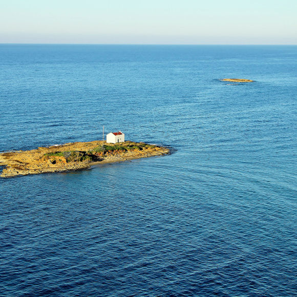 Aerial view of a small rock off the coast of Malia, Crete featuring a solitary church 