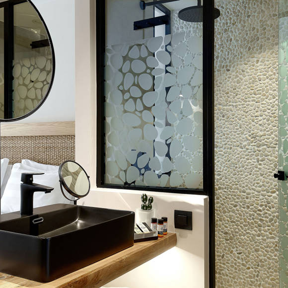 Vanity area with black sink, round mirrors and a glass shower with patterned design