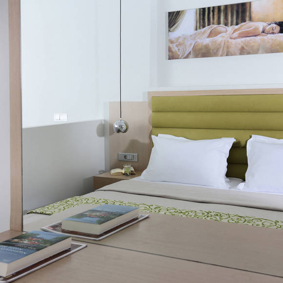 double bed with green headboard reflected in a mirror, with books on the desk