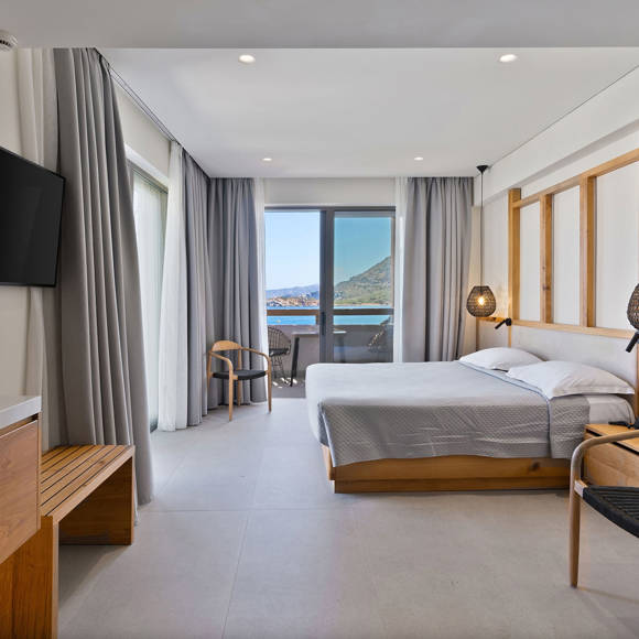Junior suite with double bed, pendant lights, wall mounted TV, wooden furniture and balcony with sea and mountain view