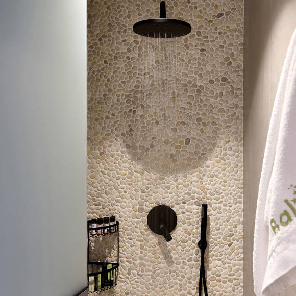 Shower area with pebble wall, black rainfall showerhead, and a towel hanging on the side