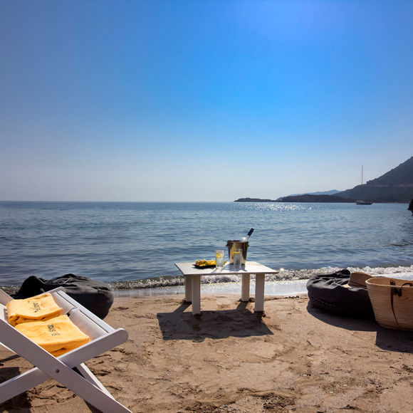 Relaxing beach setup with lounge chair, drinks on a table and sea view under a clear sky