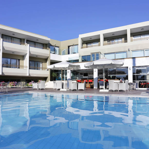 Pool surrounded by sunbeds and parasols, set against the backdrop of a hotel's building