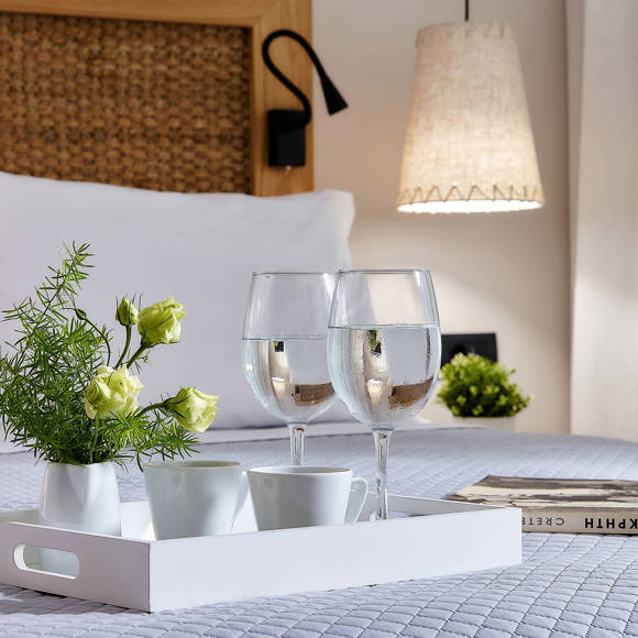 Tray with drinks, cusps and flowers on a double bed with a book beside it