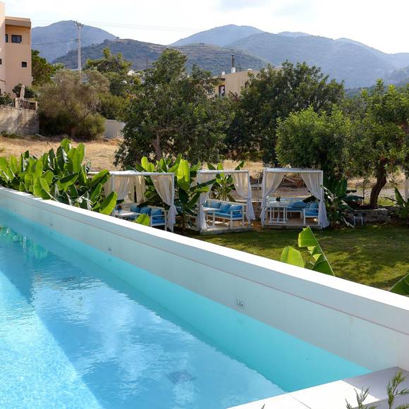 Outdoor pool with garden view, sunbeds and cabanas surrounded by greenery