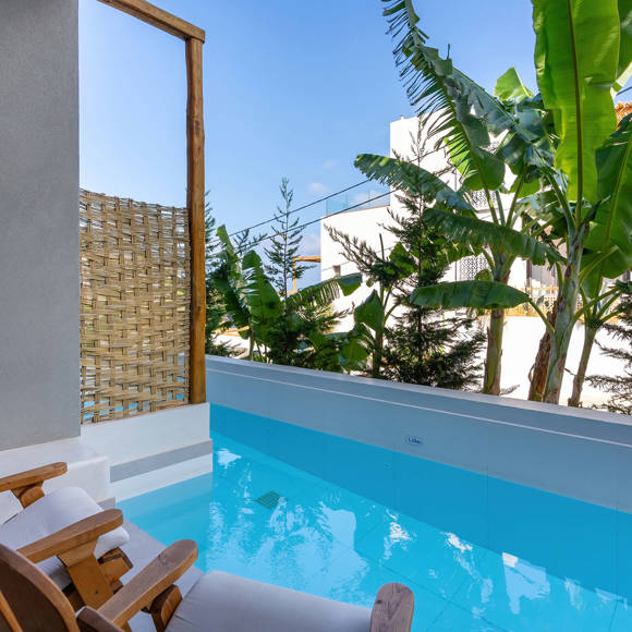 Pool with two wooden sun loungers, a partial bamboo divider and greenery in the background