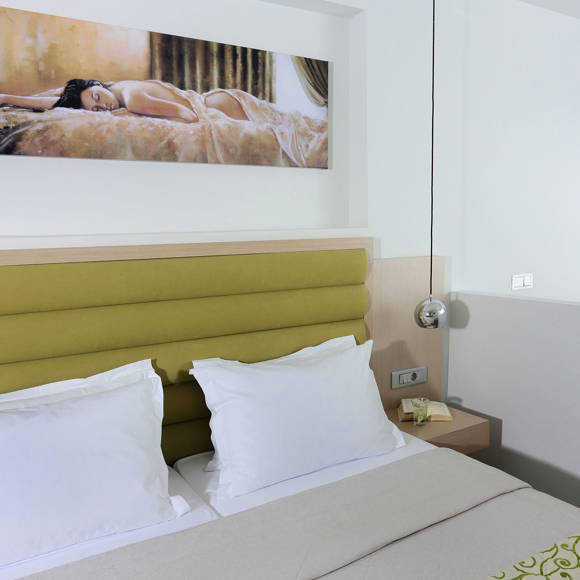 close-up of a double bed with green headboard, white pillows and wall art above