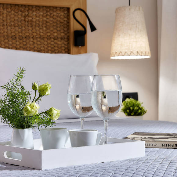 Tray with drinks, cups and flowers on a double bed with a woven headboard and a book beside